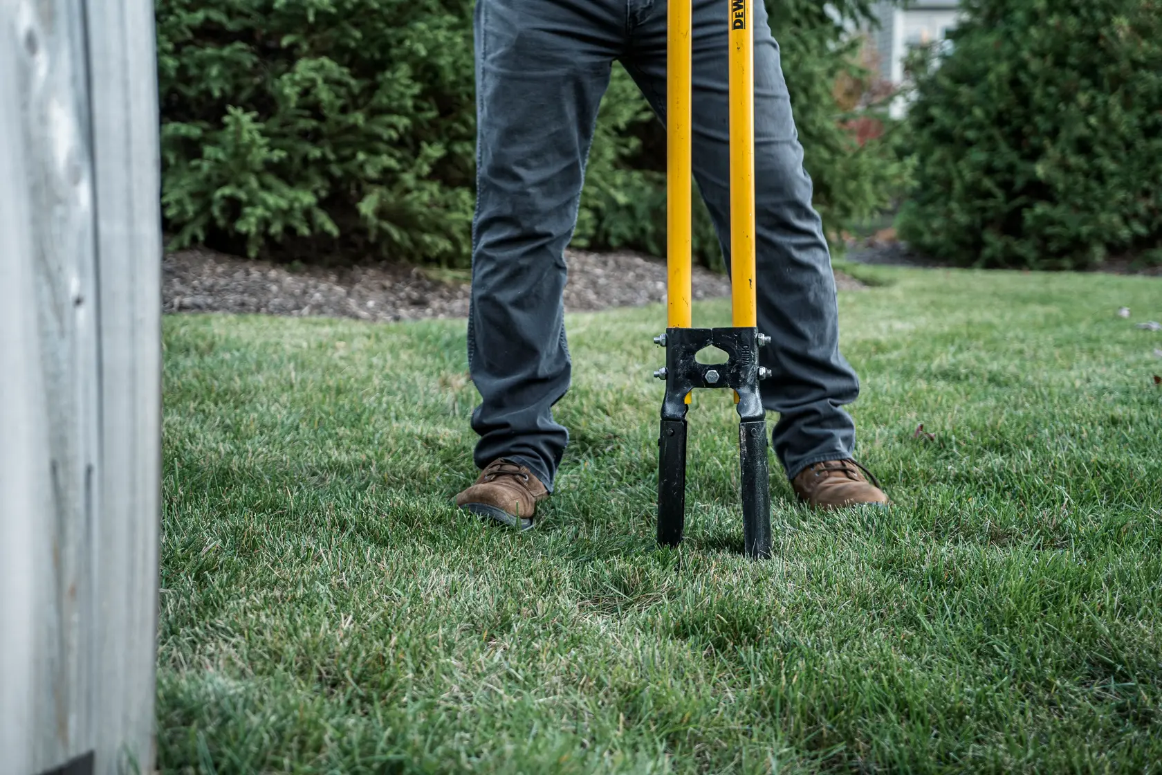 46 inch Fiberglass Handle Post Hole Digger in front view making holes in grass in gray pants and boots