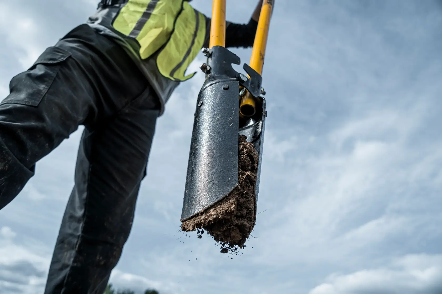 46 inch Fiberglass Handle Post Hole Digger close up removing dirt from hole in safety vest
