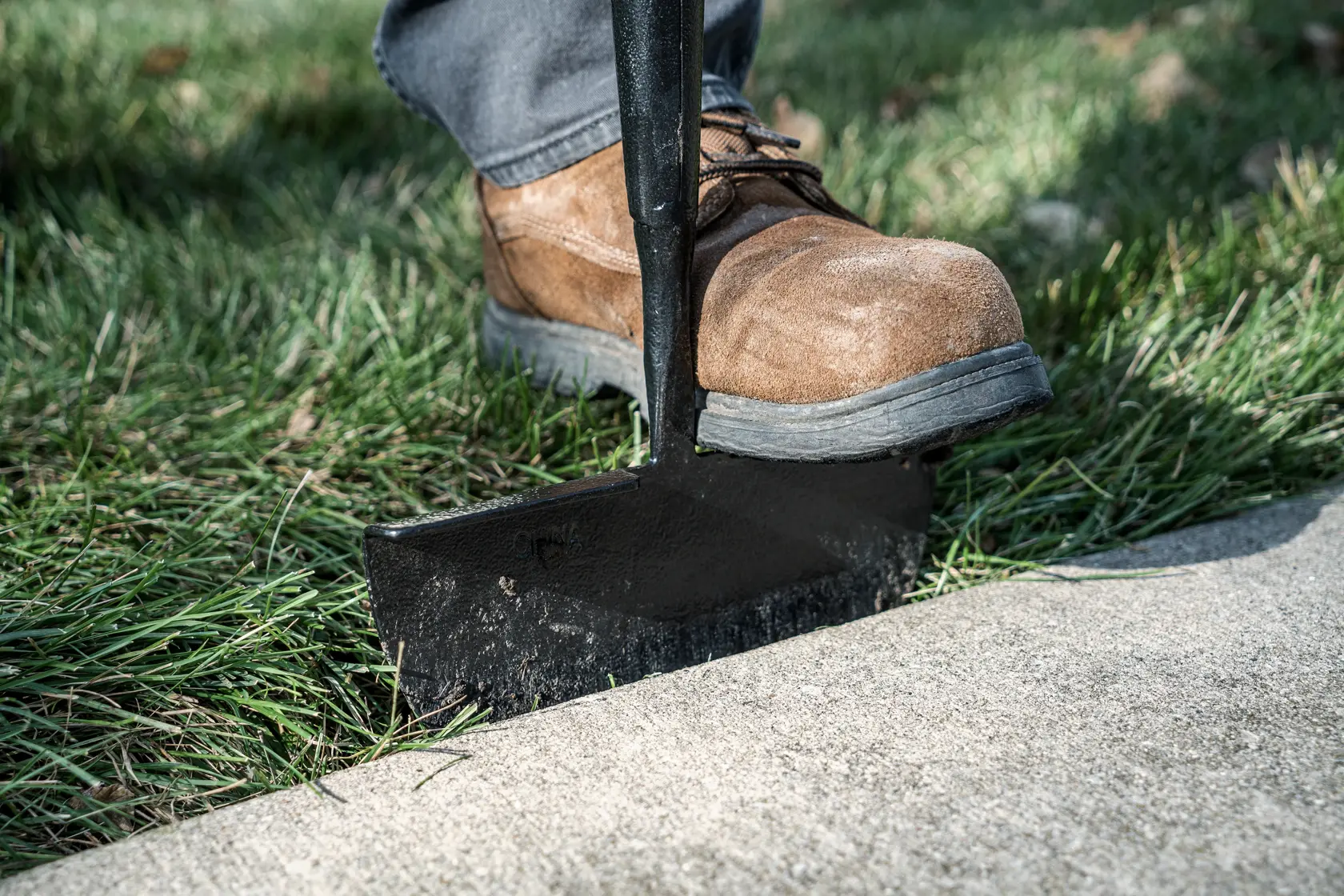 55 inch Wood Handle Turf Edger close up being pushed into grass in work boots