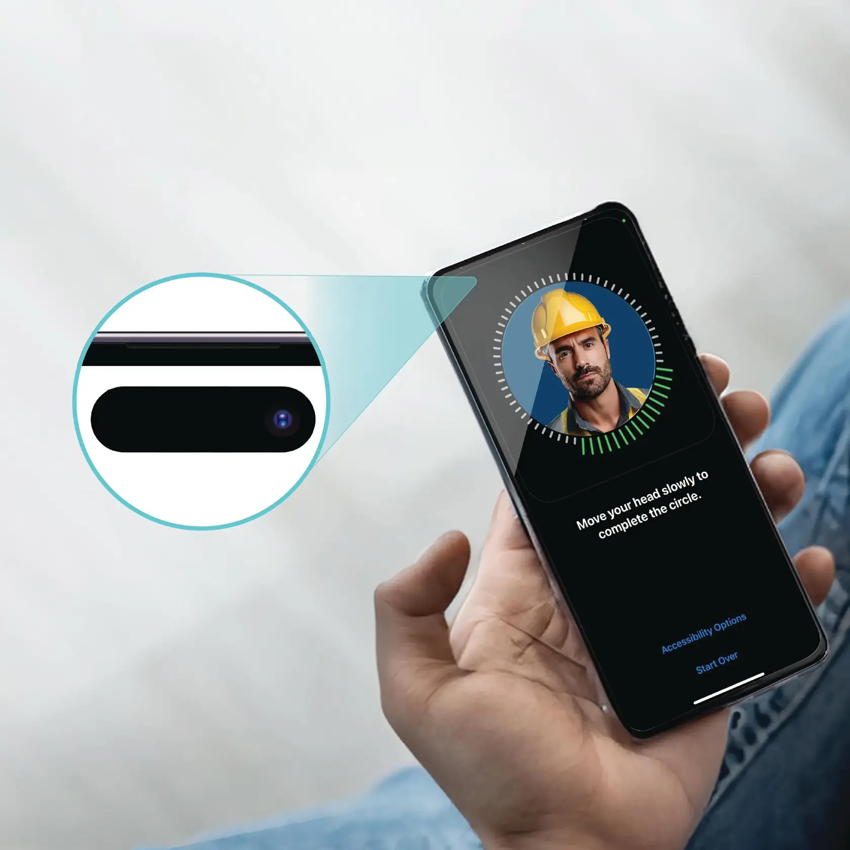 A person holding a smartphone, which is displaying a facial recognition setup screen. The screen shows a blurred face wearing a yellow safety helmet, with instructions to move the head slowly to complete the circle. There is a close-up of the phone's camera highlighted in the image.