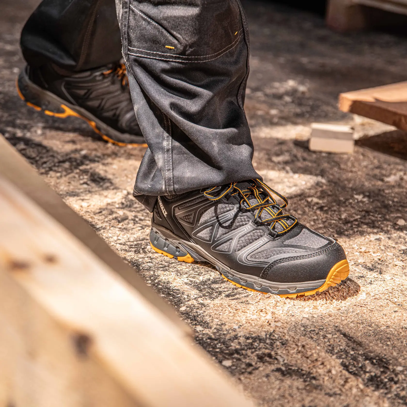 Side view facing right of the DEWALT Boron Safety Toe Work Shoe in black/yellow on model on location