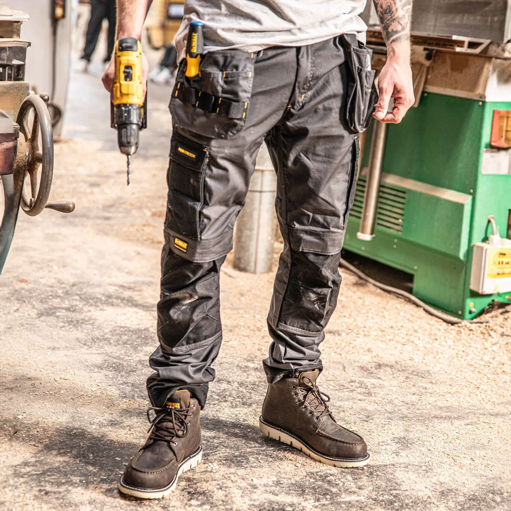 Front view of the DEWALT Barstow men’s work pants in grey/black on model on location
